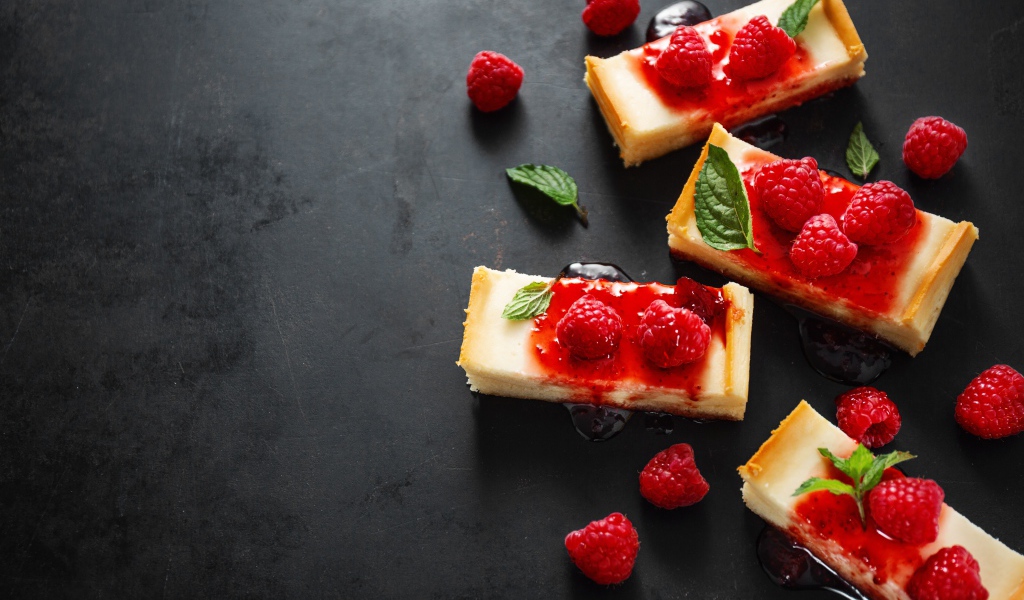 Pieces of cheesecake on a table with jam and raspberries