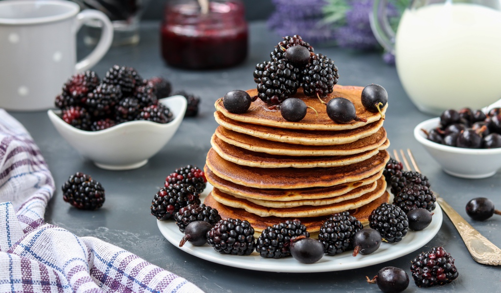 Румяные оладьи на тарелке с ягодами черники и смородины