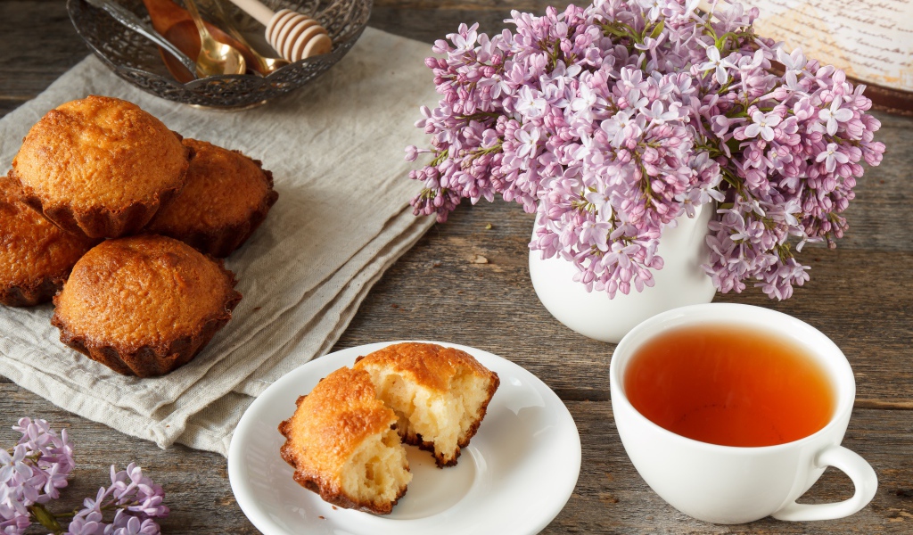 Сладкие кексы на столе с чаем и букетом сирени