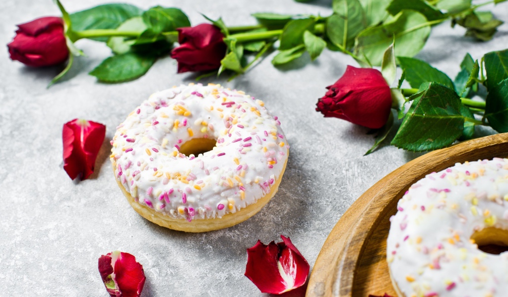 Сладкий пончик с глазурью на столе с красными розами