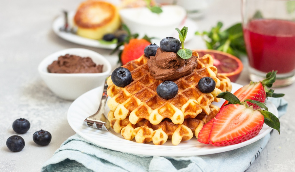 Сладкая вафля с шоколадом, ягодами черники и клубники на тарелке