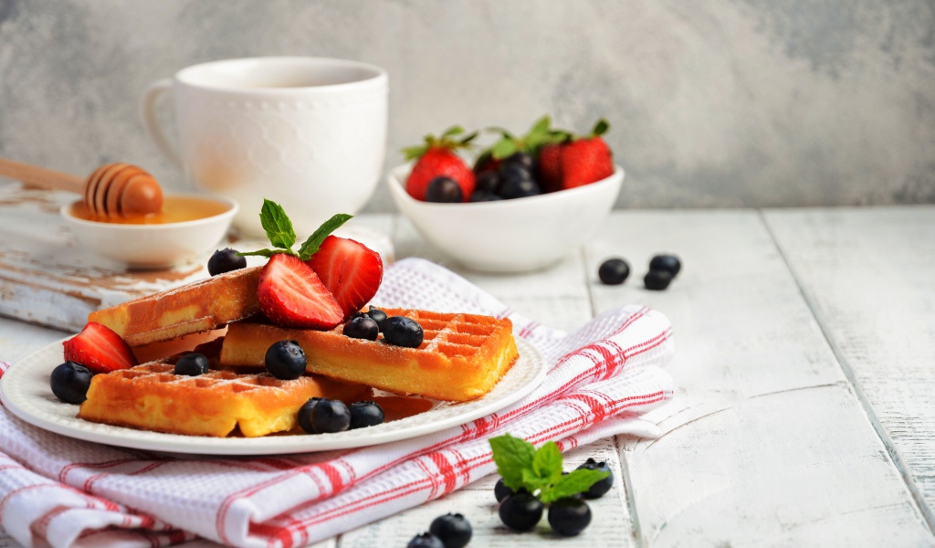 Сладкие вафли с ягодами черники и клубники на столе с медом и чаем