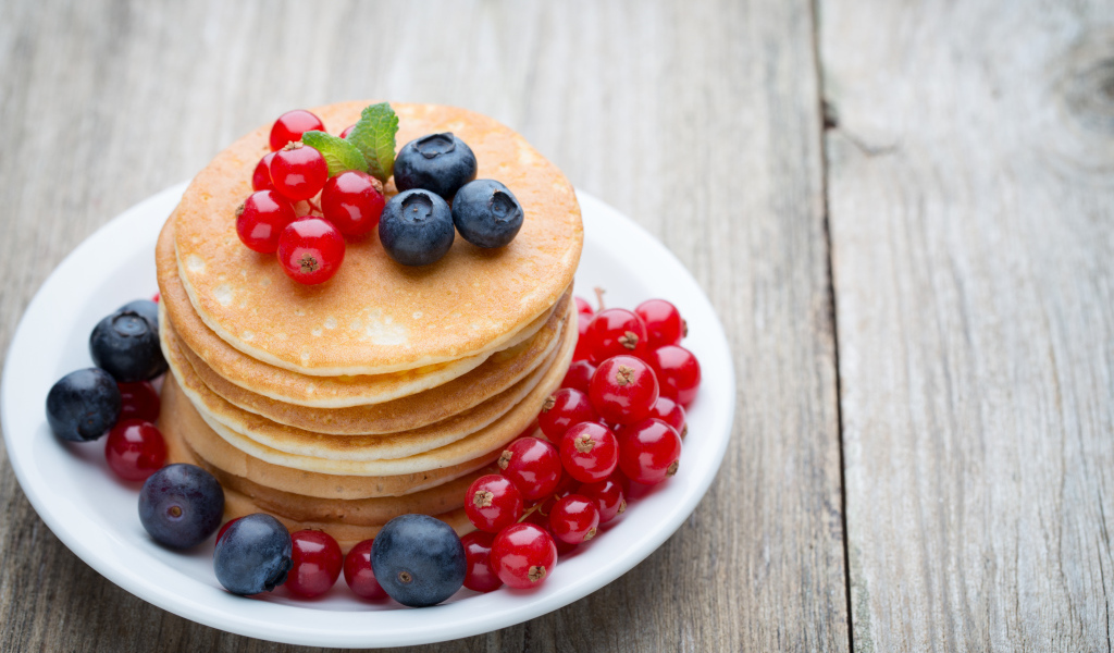Вкусные оладьи на тарелке с ягодами красной смородины и черники