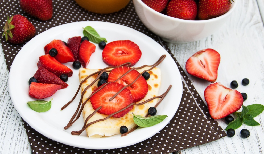 Тонкий блинчик на тарелке с шоколадом, ягодами клубники и черники