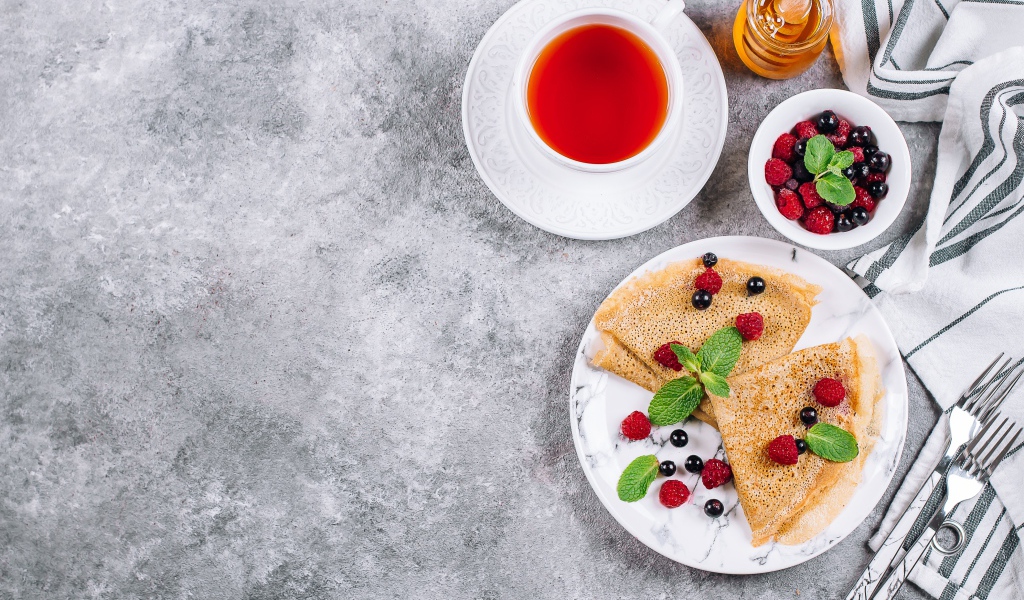 Тонкие блинчики на столе с ягодами, чаем и медом