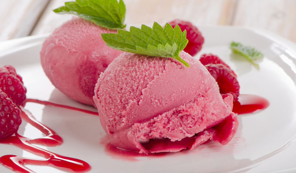 Два шарика малинового мороженого на тарелке с ягодами 