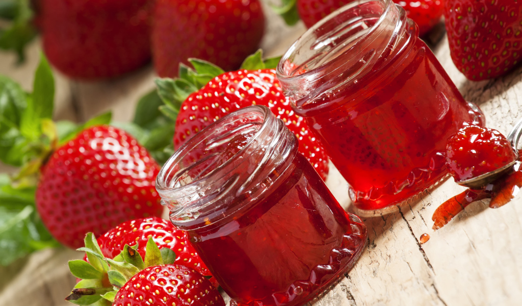 Две баночки клубничного джема на столе с клубникой