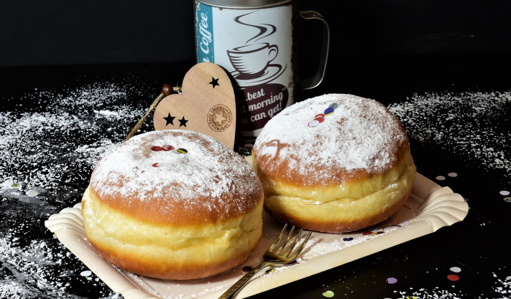 Два пышных пончика с сахарной пудрой на черном столе с кофе