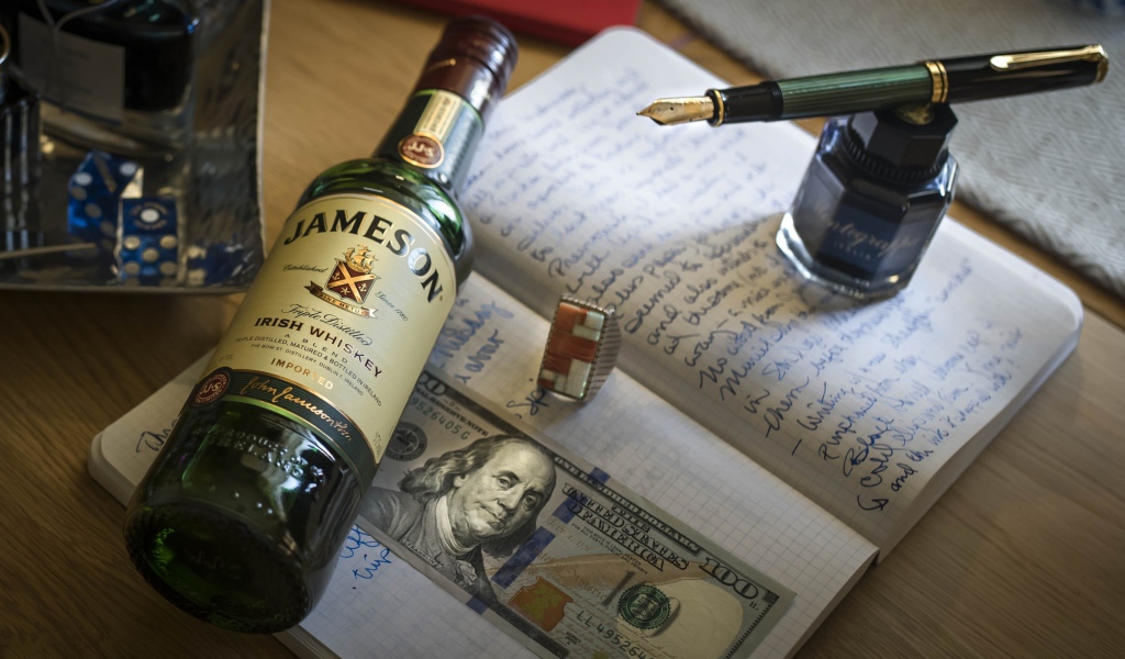 Бутылка виски лежит на тетради с чернильницей и купюрой
