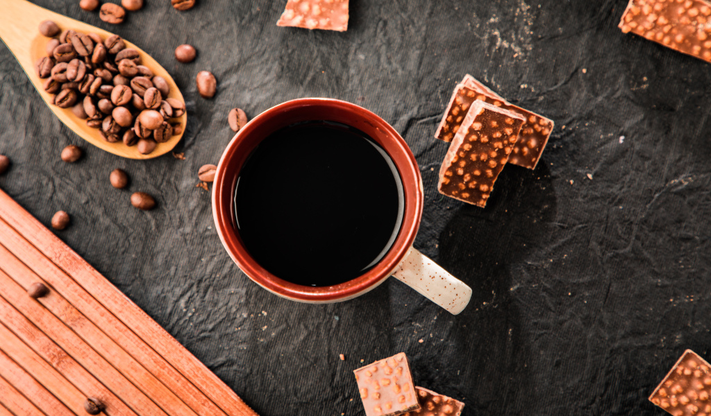 Чашка кофе на столе с кусочками шоколада и кофейными зернами