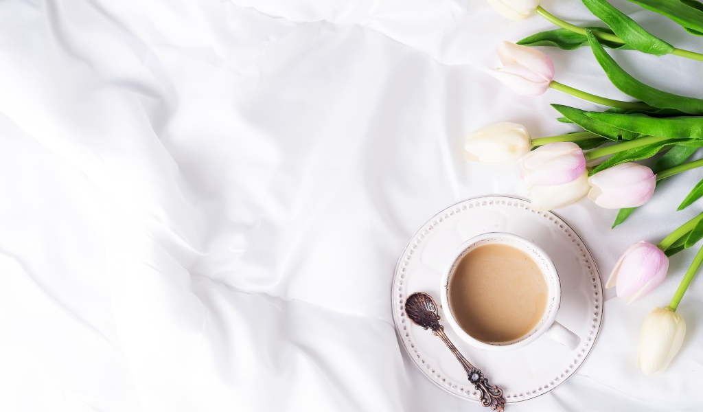 Чашка кофе на белом покрывале с тюльпанами