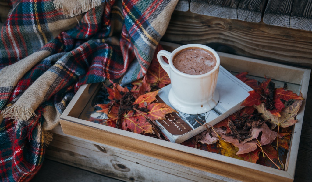 Чашка кофе стоит на книге на ступеньках с пледом