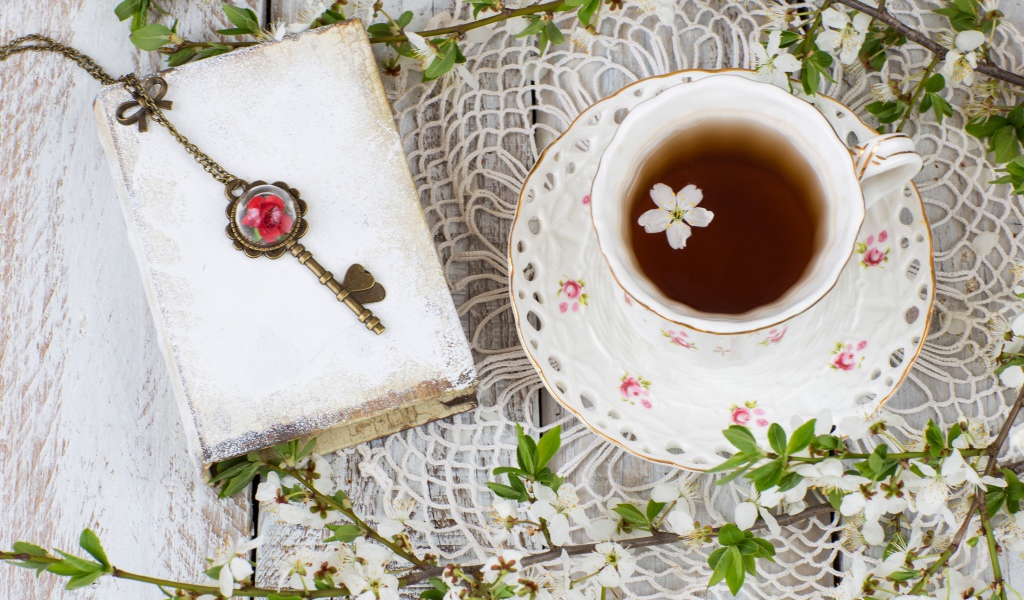 Чашка чая на столе с книгой и белыми цветами вишни 
