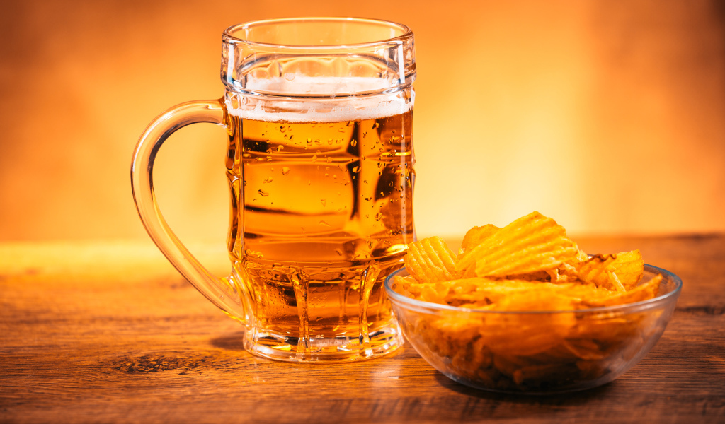 Бокал пива с тарелкой чипсов на столе 