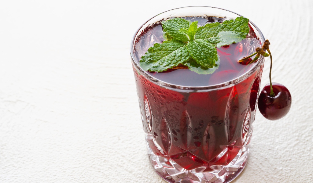 Стакан вишневого сока с мятой на белом фоне