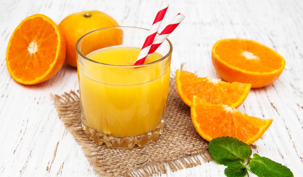 Стакан свежего сока на столе с апельсинами