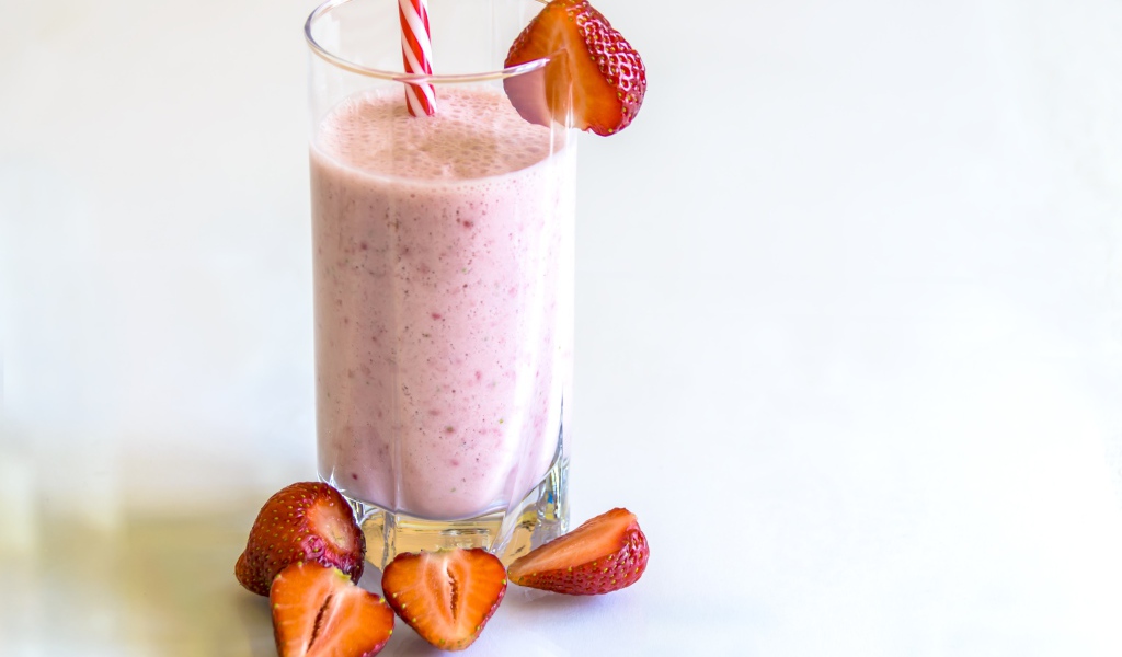 Стакан клубничного смузи на белом фоне с ягодами