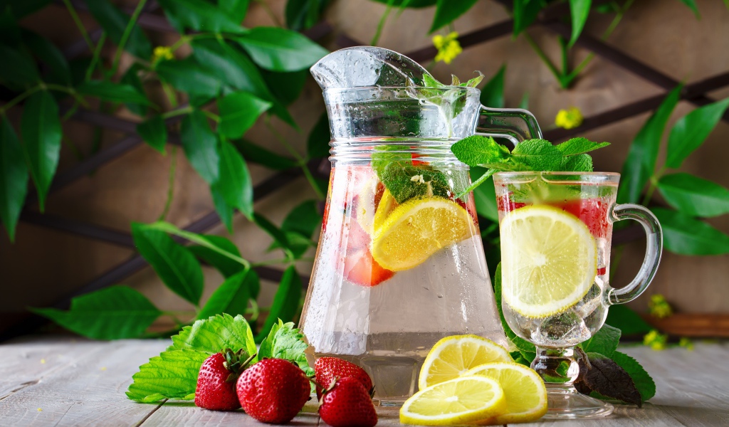 Холодный мохито в графине на столе с клубникой и лимоном