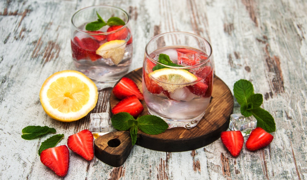 Холодный мохито на столе с ягодами клубники, лимоном и мятой