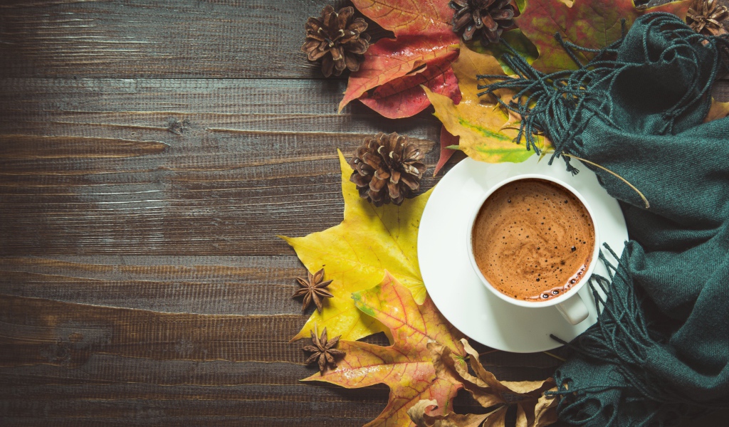 Чашка кофе на столе с шарфом, желтыми листьями и шишками