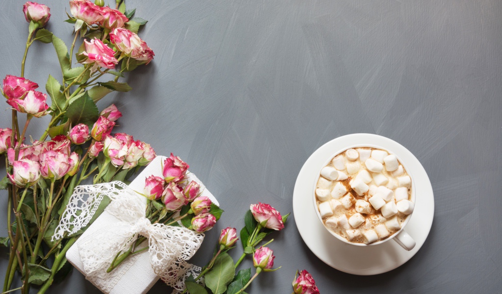 Чашка кофе с маршмеллоу на столе с подарком и букетом роз