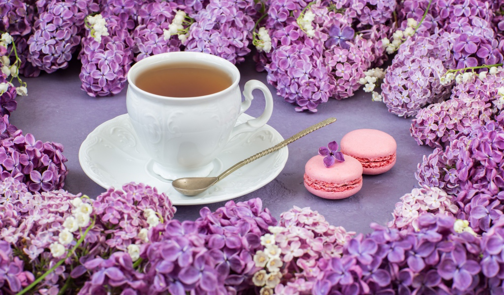 Чашка чая на столе с цветами сирени и десертом макарон