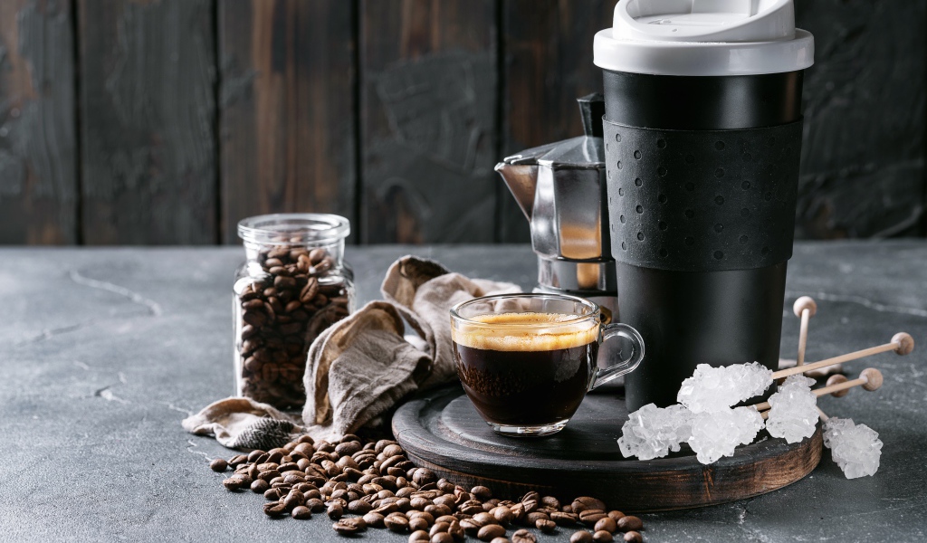 Стеклянная чашка кофе на столе с термосом и зернами