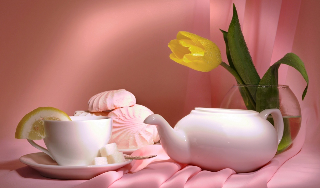 Чайник на столе с чашкой, зефиром и желтым тюльпаном