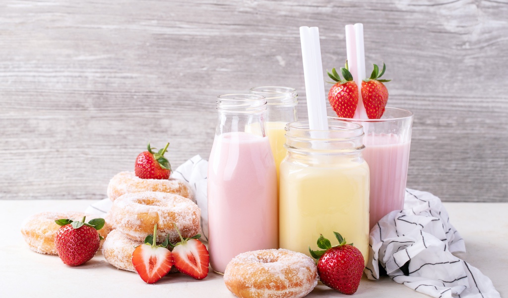 Молочные коктейли на столе с пончиками и ягодами клубники 