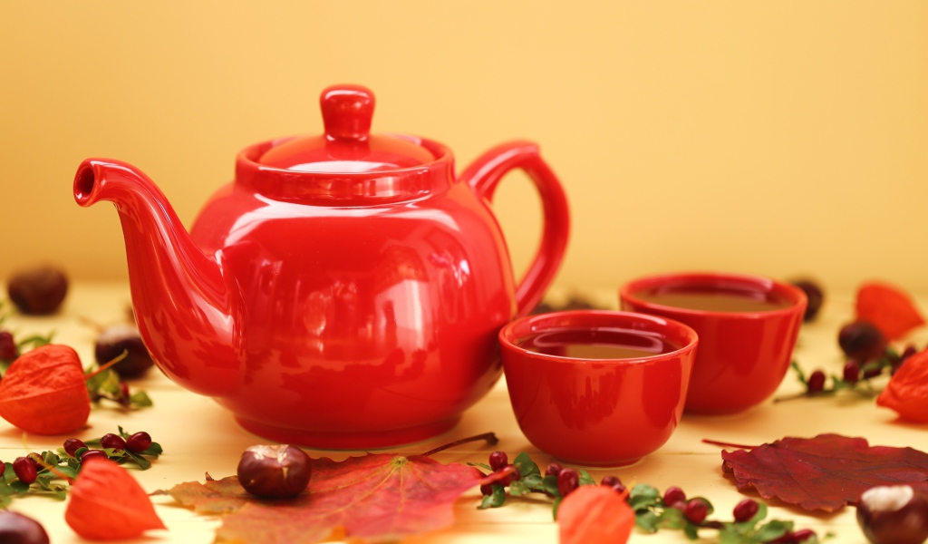 Красный чайник с чашками на столе осенью 