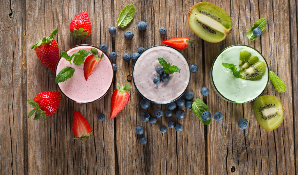 Стаканы со смузи на столе с киви, ягодами клубники и черники