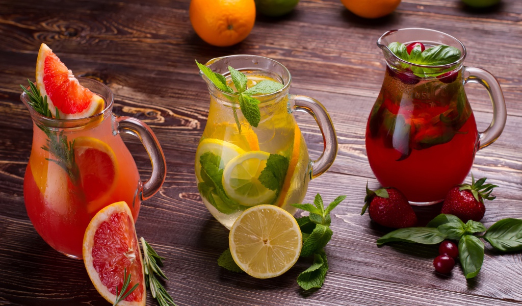 Три стеклянных графина с напитком на деревянном столе с фруктами