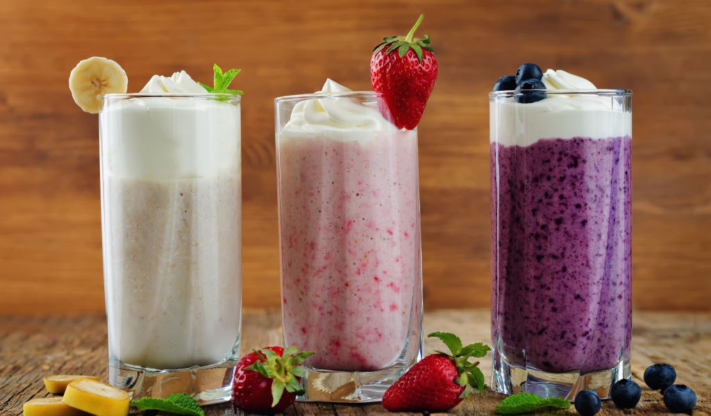 Три стакана смузи со сливками на столе с ягодами