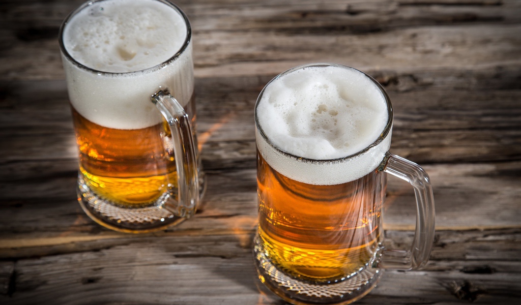 Два бокала пива с пеной на деревянном столе