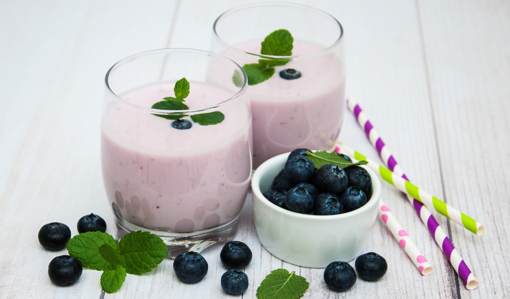 Два стакана коктейля в стаканах на столе с ягодами черники и трубочками