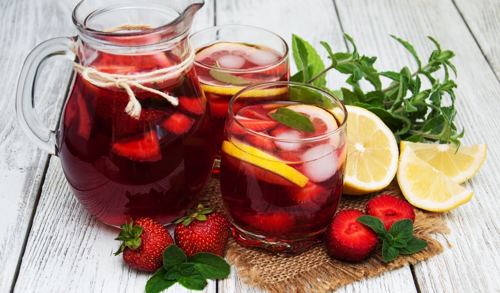 Два стакана мохито на столе с графином, лимоном, клубникой и мятой