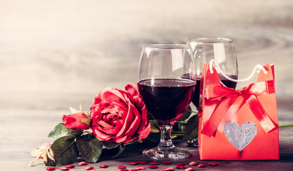 Два бокала красного вина на столе с розой и подарком 