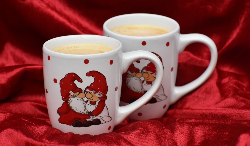 Две белые чашки кофе с рисунком стоят на красной ткани