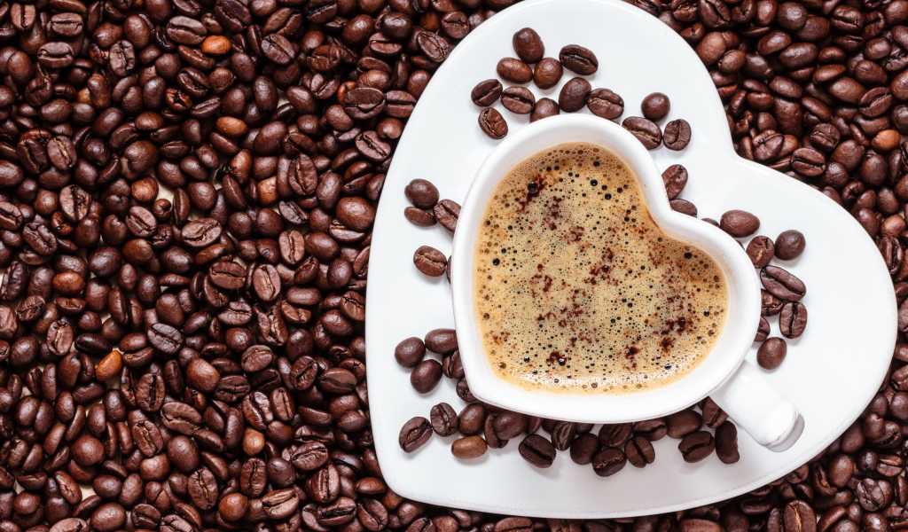 Белая чашка в форме сердца стоит на кофейных зернах 