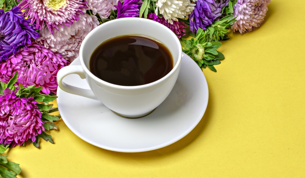 Белая чашка кофе на желтом фоне с букетом цветов астры