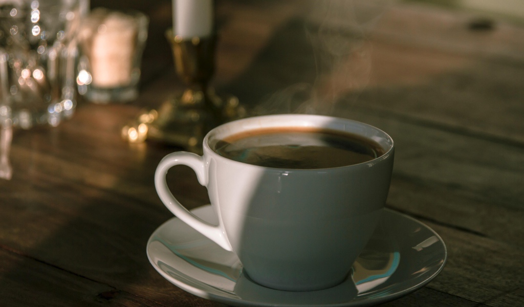 Белая чашка кофе на столе в лучах солнца