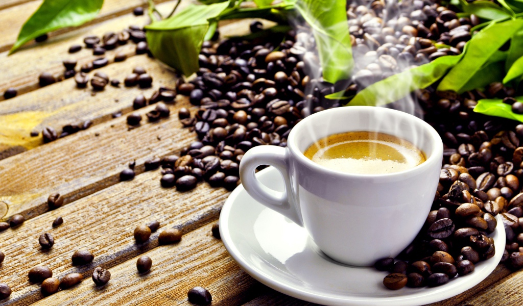 Белая чашка с горячим кофе на деревянном столе с кофейными зернами