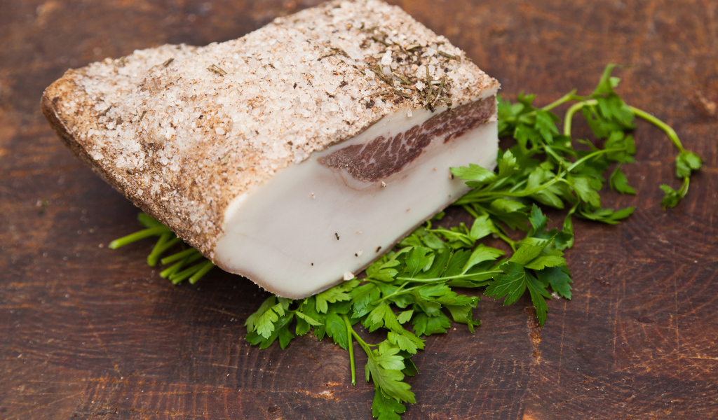 Кусок сала со специями на столе с зеленью петрушки