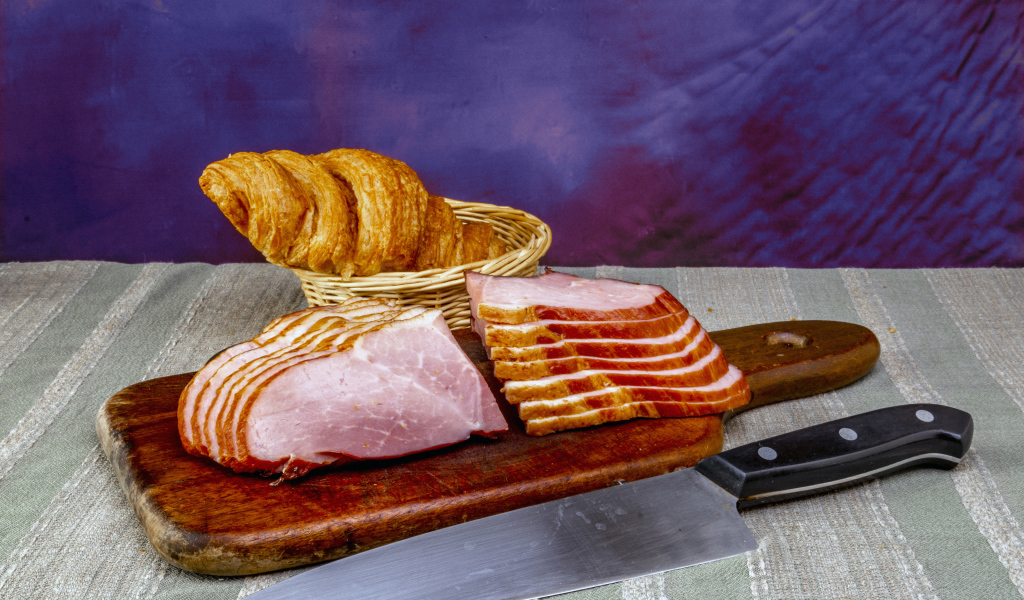 Кусок нарезанной ветчины на доске с круассаном