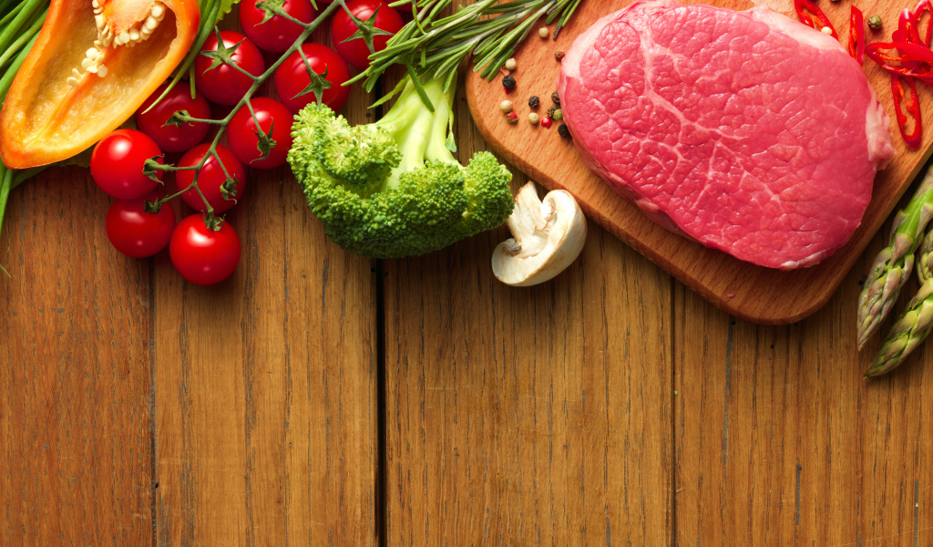 Кусок свежего мяса на столе с овощами и зеленью 