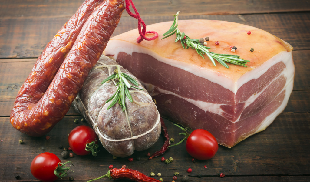 Кусок мяса и колбаса на деревянном столе с помидорами и специями
