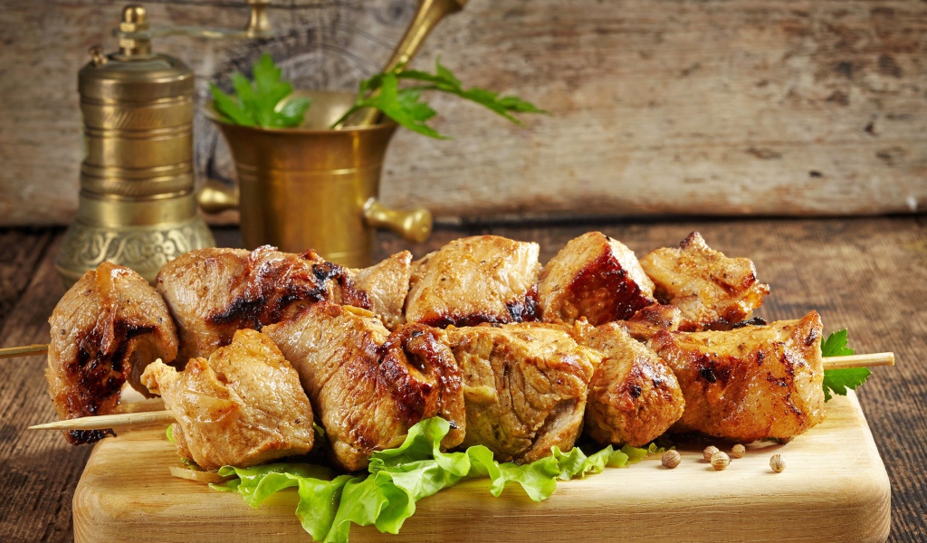 Аппетитный шашлык лежит на разделочной доске с листьями салата