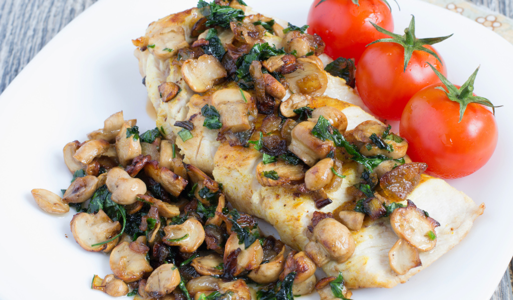 Аппетитный кусок куриного филе с грибами на тарелке с помидорами 