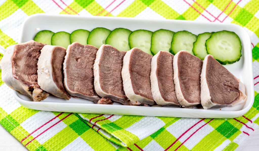 Вареный язык на тарелке со свежими огурцами