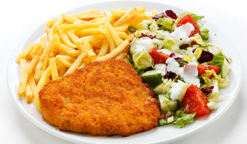 Отбивная с картофелем фри и салатом на большой белой тарелке